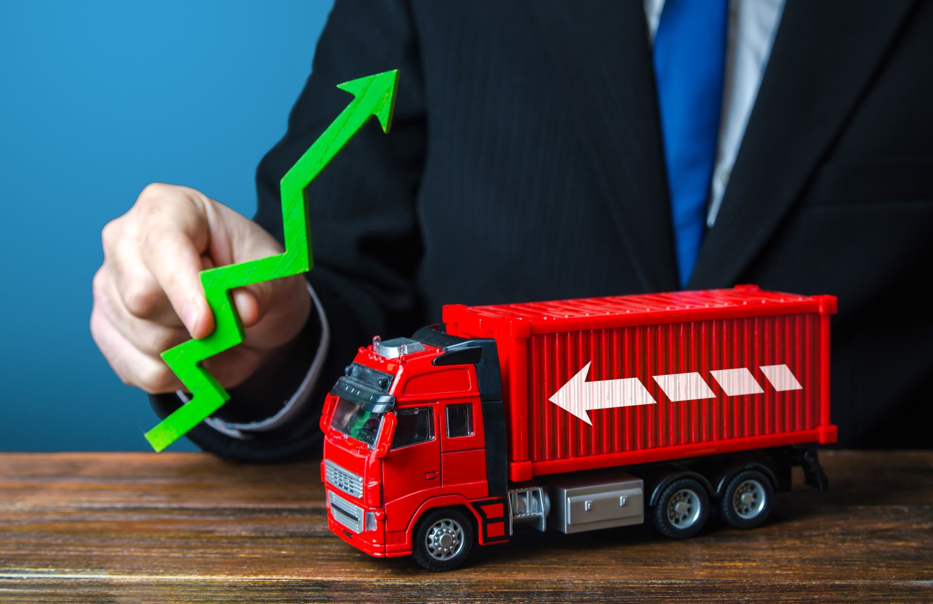 L’homme d’affaires tient une flèche verte et un camion. Croissance de la production. Importer, exporter. Fin de la crise de pénurie de conteneurs. Inflation du transport, tarifs d’expédition élevés. Augmentation des prix. Augmentation du trafic.